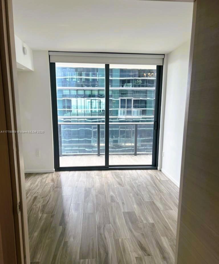 A small, empty room features light wood-look flooring, white walls, and a large sliding glass door — 801 S Miami Ave # 5108, Miami FL 33130, MIAMI, FL