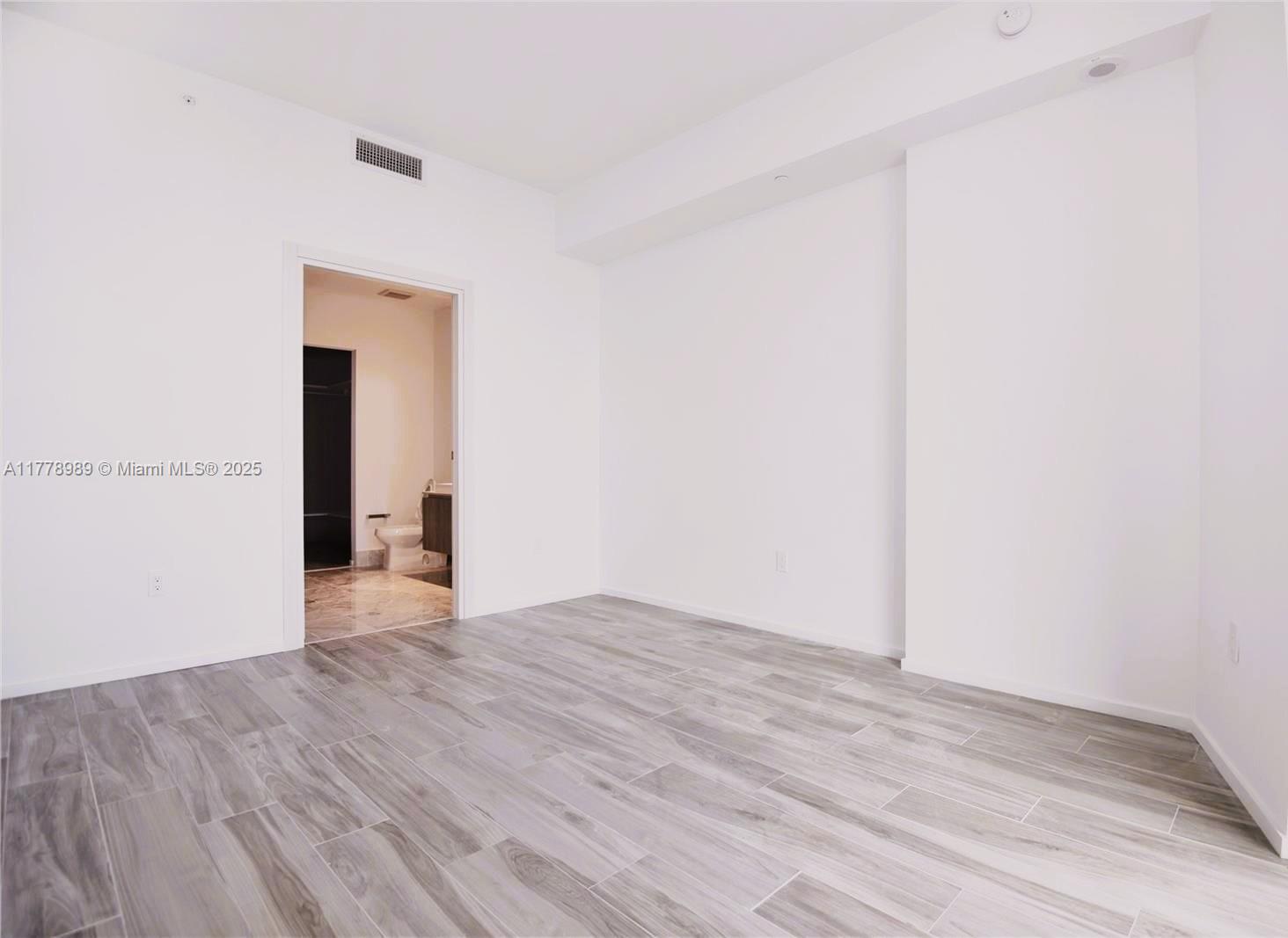 A bright, empty room features light gray wood-look tile flooring and a doorway to a bathroom — 801 S Miami Ave # 5108, Miami FL 33130, MIAMI, FL