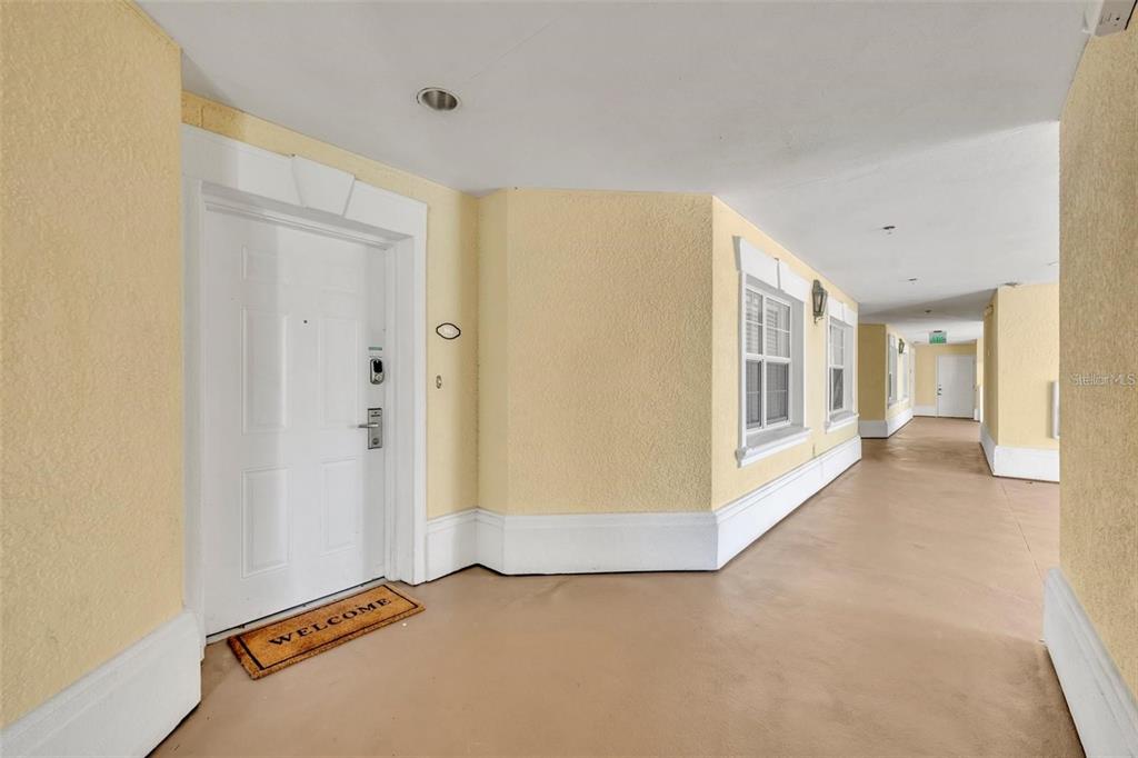 A covered outdoor walkway leads to a white front door with a welcome mat — 7659 WHISPER WAY UNIT 102, REUNION, FL