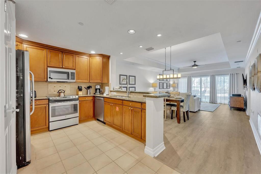 A kitchen with wood cabinets and tile floors opens into a dining area and living room — 7659 WHISPER WAY UNIT 102, REUNION, FL