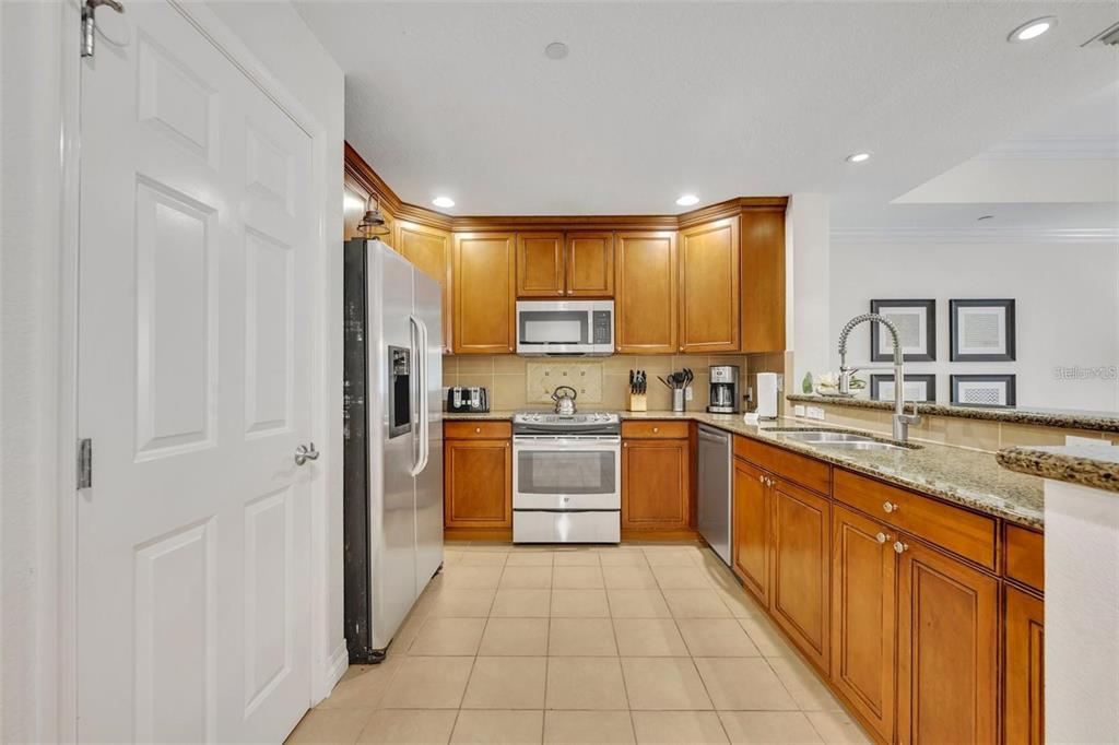 A kitchen features wood cabinets, stainless steel appliances, granite countertops, and light-colored tile flooring — 7659 WHISPER WAY UNIT 102, REUNION, FL