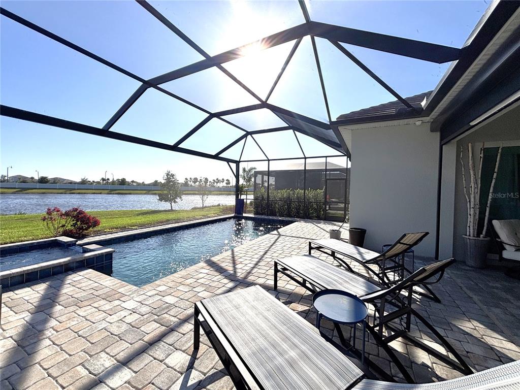A screened-in patio features a swimming pool, lounge chairs, and a view of a lake — 17510 JADESTONE COURT, VENICE, FL