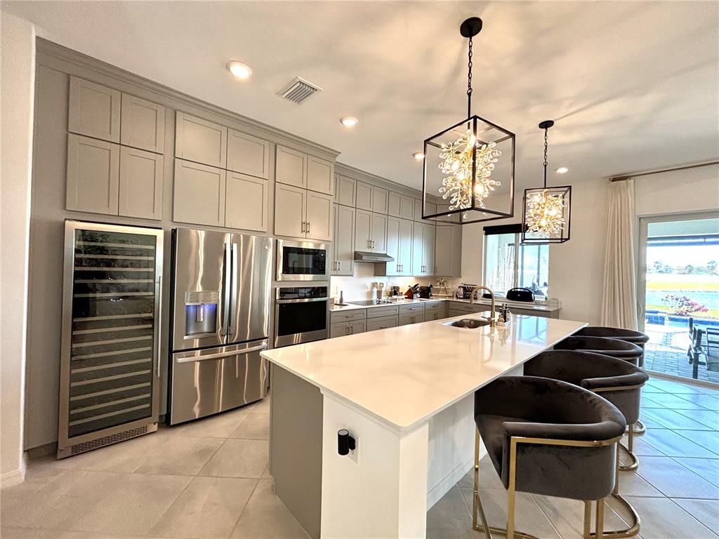 A modern kitchen features light gray cabinetry, stainless steel appliances, and a large white island — 17510 JADESTONE COURT, VENICE, FL