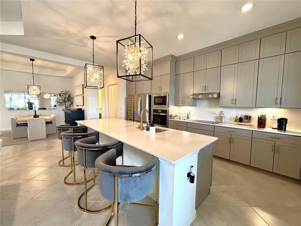 A modern kitchen features a large island with bar stools, gray cabinetry, and pendant lighting — 17510 JADESTONE COURT, VENICE, FL