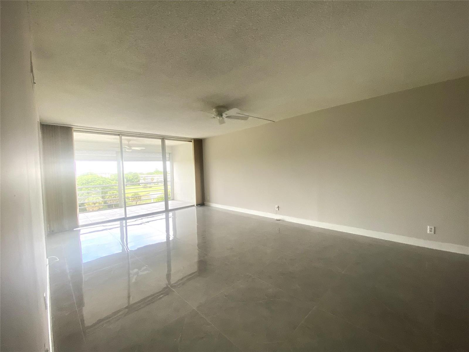 An empty living room features large gray floor tiles, a ceiling fan, and sliding glass doors — 2671 S Course Drive # 602, Pompano Beach FL 33069, POMPANO BEACH, FL