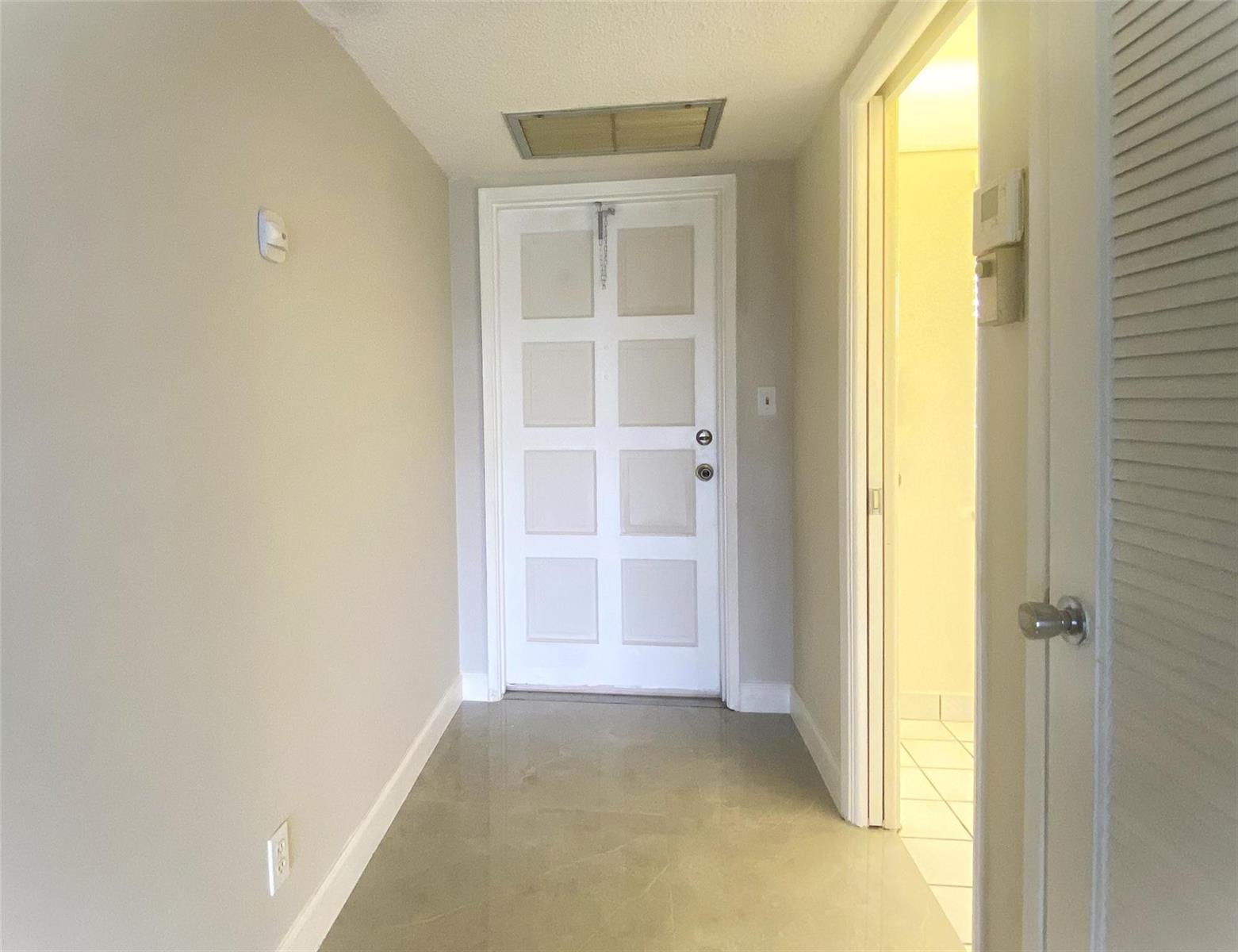 A hallway with light-colored walls, tile flooring, a white paneled door, and an open doorway — 2671 S Course Drive # 602, Pompano Beach FL 33069, POMPANO BEACH, FL