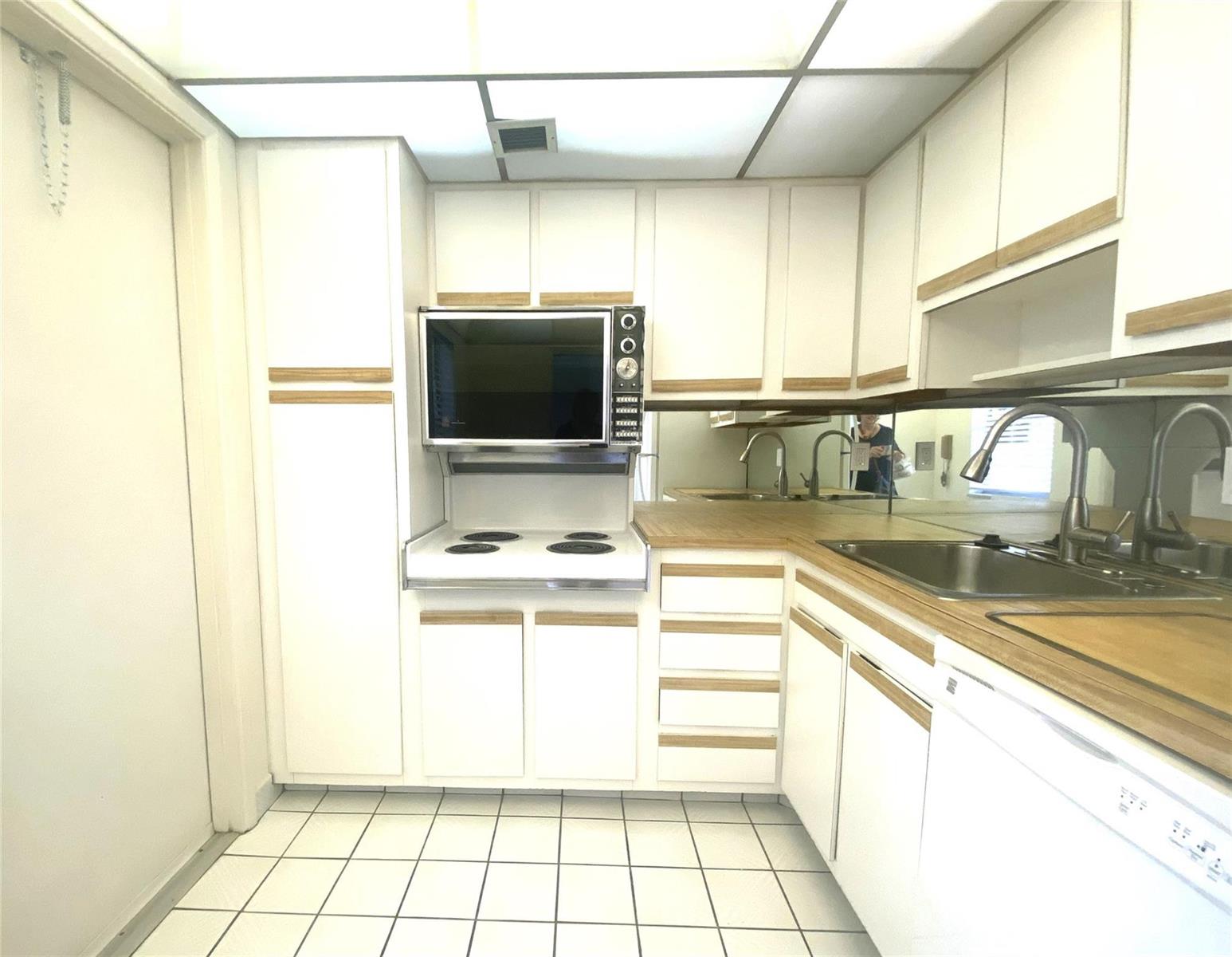 A kitchen features white cabinets with wood trim, a mirrored backsplash, and white tile flooring — 2671 S Course Drive # 602, Pompano Beach FL 33069, POMPANO BEACH, FL