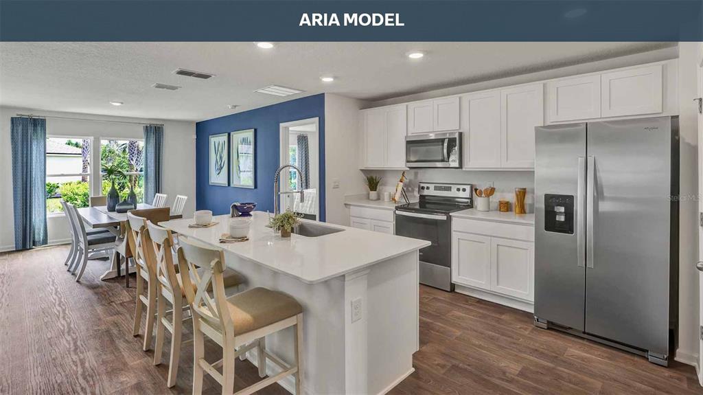 A kitchen features a white island, stainless steel appliances, white cabinets, and wood-look flooring — 77 SAWDUST LANE, PALM COAST, FL