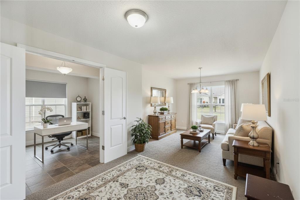 A living room with carpeted floors opens into a tiled home office through double doors — 545 VICEROY COURT, KISSIMMEE, FL