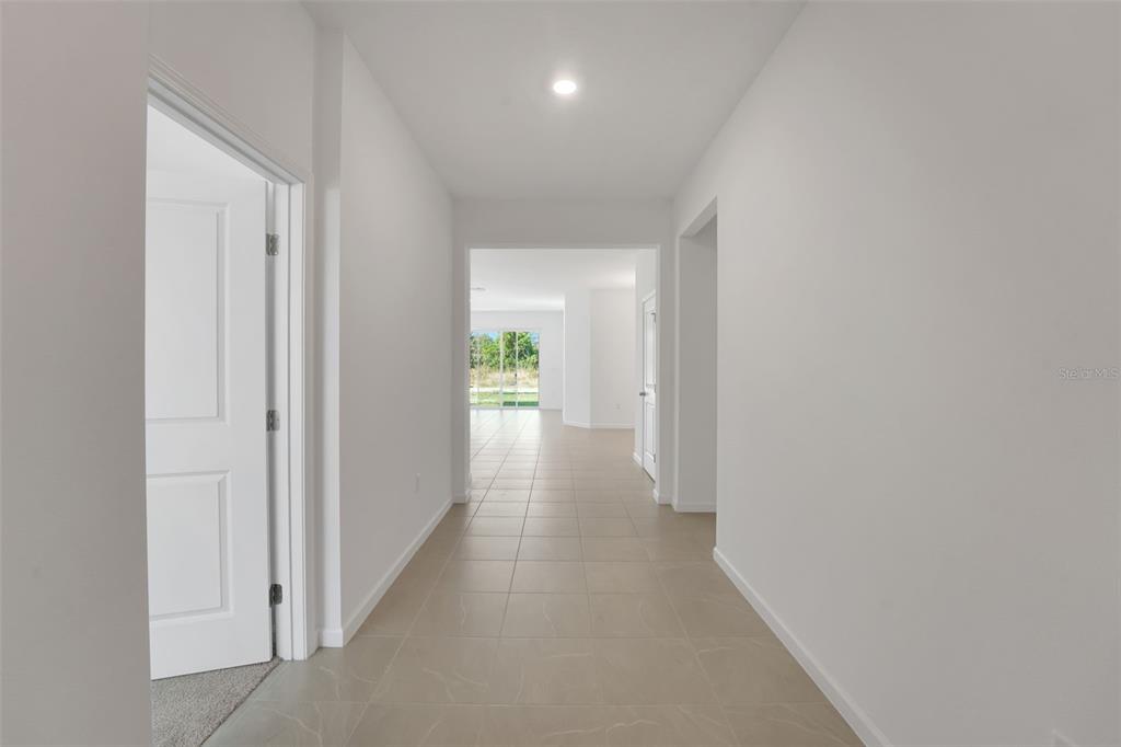 A hallway with light-colored tile flooring leads toward an open living area with sliding doors — 1052 LUKE AVENUE, WINTER HAVEN, FL