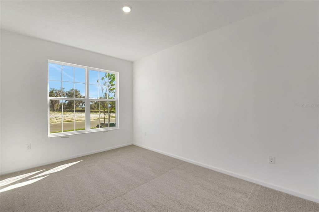 An empty bedroom features white walls, beige carpeting, and a window overlooking a vacant lot — 1052 LUKE AVENUE, WINTER HAVEN, FL