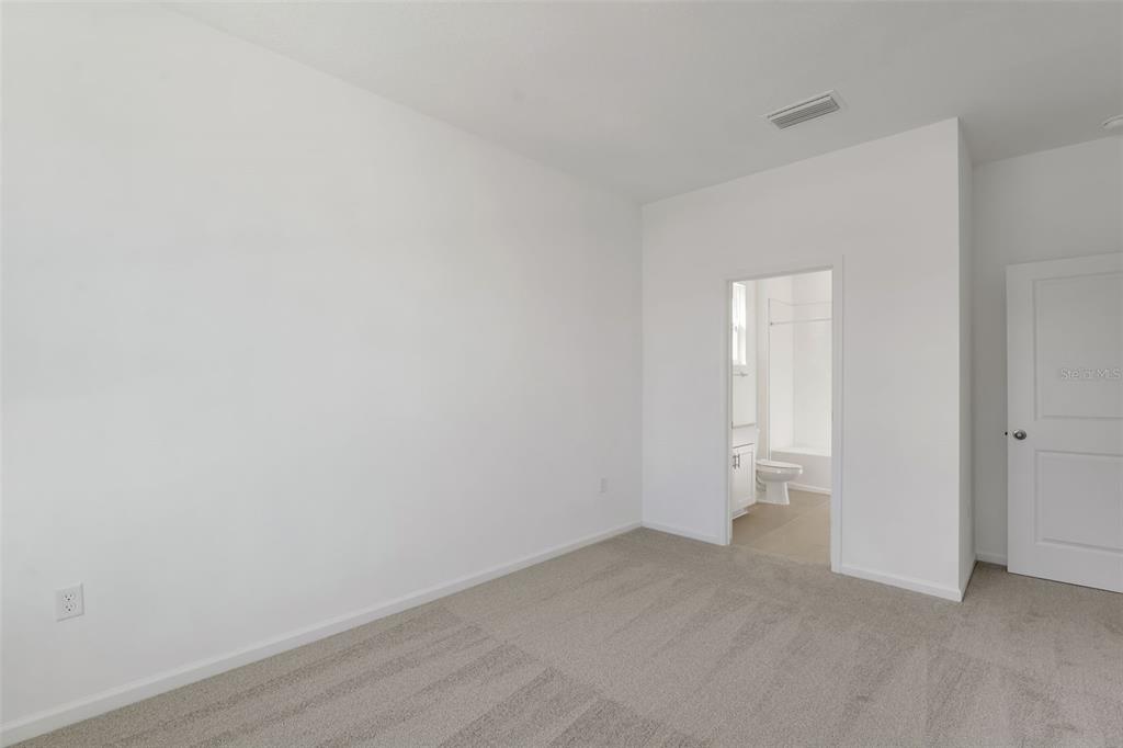 A carpeted bedroom features white walls, a doorway to an attached bathroom, and a door — 1052 LUKE AVENUE, WINTER HAVEN, FL