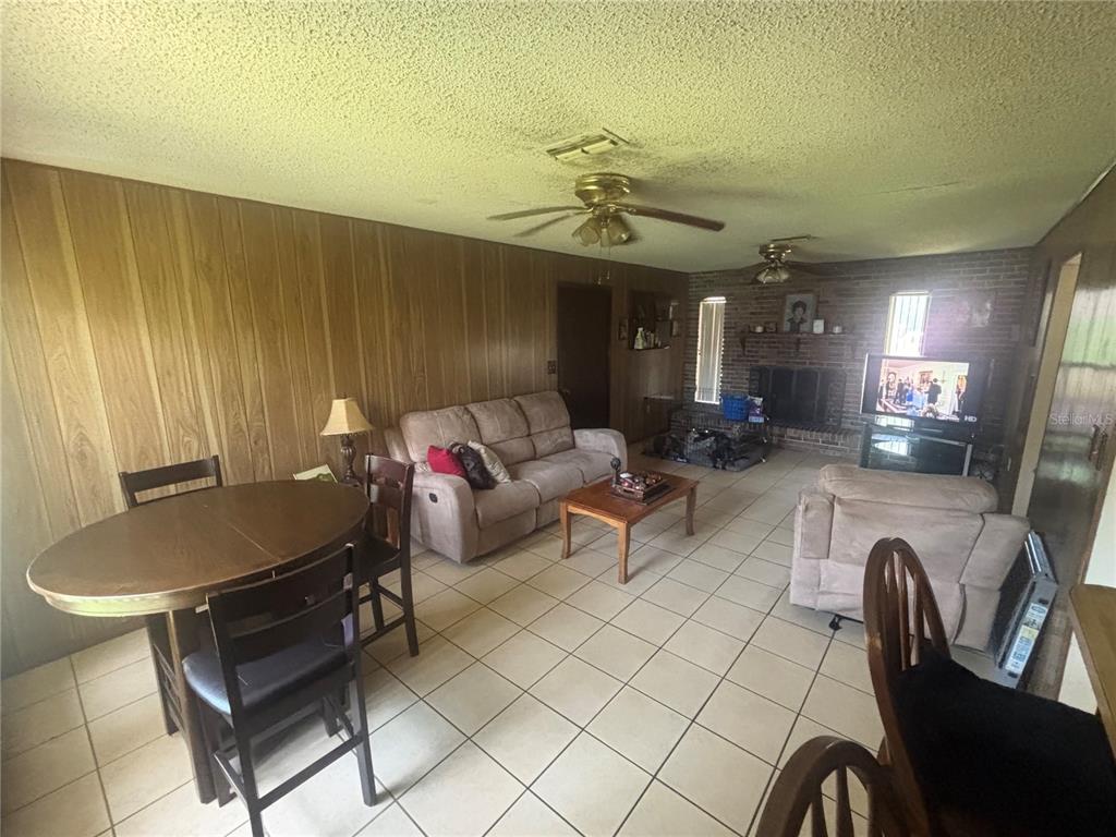 A living room with wood-paneled walls, tile flooring, a brick fireplace, and a dining area — 2105 SW 5TH STREET, OCALA, FL
