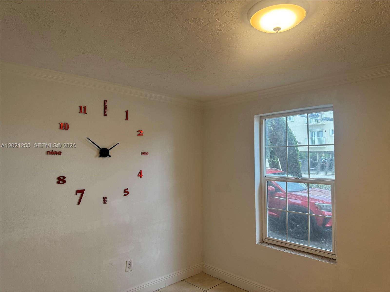 A room features a large wall-mounted clock, a window overlooking a red car, and a ceiling light — 11 SW 32nd Ave # 1, Miami FL 33135, MIAMI, FL