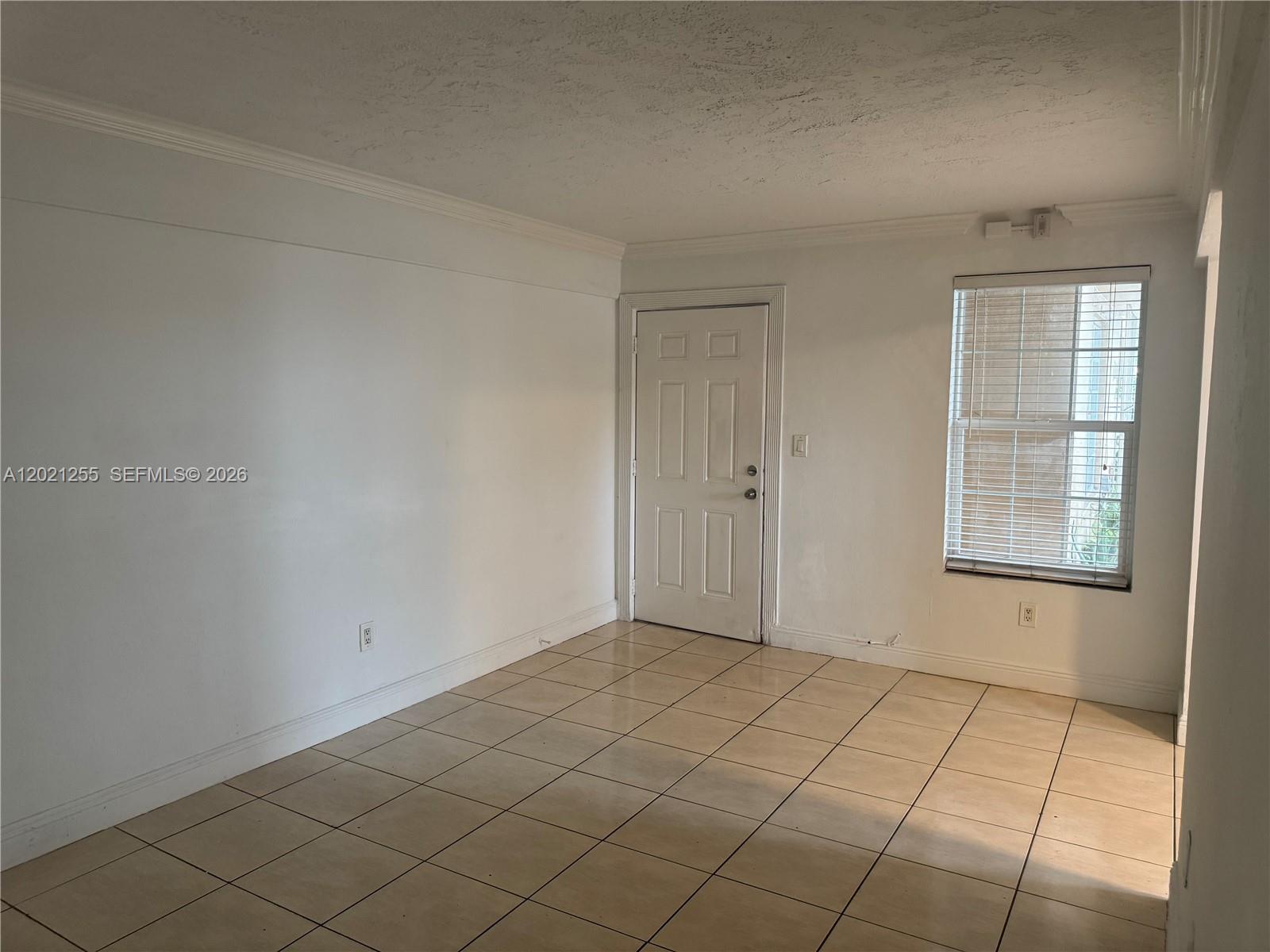 An empty room features white walls, beige tile flooring, a white door, and a window — 11 SW 32nd Ave # 1, Miami FL 33135, MIAMI, FL