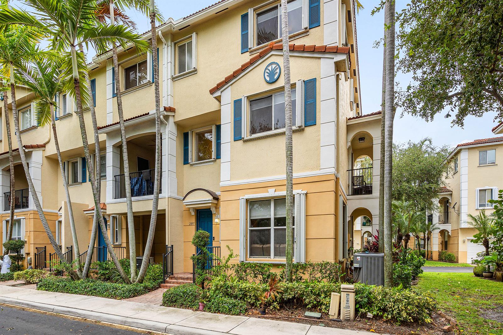 A three-story yellow townhouse with blue shutters, a front entrance, and tall palm trees — 2897 S Greenleaf Circle, Boynton Beach FL 33426, BOYNTON BEACH, FL