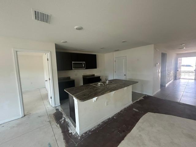 An open kitchen features dark cabinets, a granite-topped island, and unfinished concrete flooring — 24528 NW 7TH LANE, NEWBERRY, FL