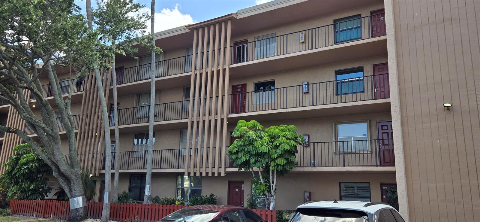 A three-story apartment building with brown stucco walls, exterior walkways, and a red fence — 7300 Lake Cir Drive # 107, Margate FL 33063, MARGATE, FL