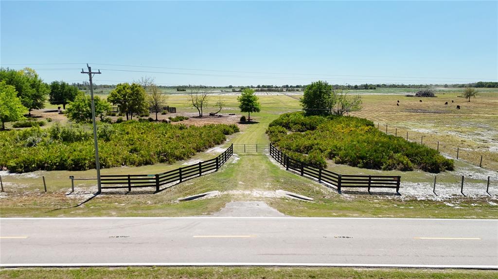 A paved road leads to a gated entrance of a fenced rural property with trees — AVON PARK CUTOFF ROAD, FORT MEADE, FL