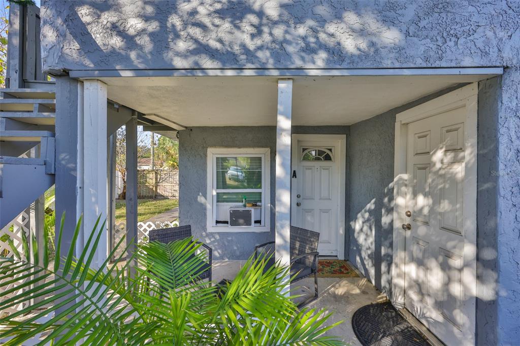 A covered porch features two chairs, a window with an air conditioner, and two white doors — 1208 17TH ST N, ST PETERSBURG, FL