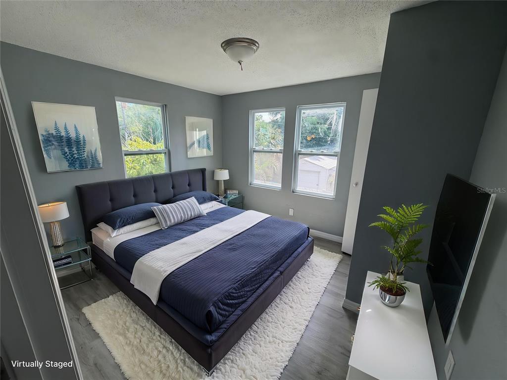 A virtually staged bedroom features a dark blue bed, gray walls, and light wood flooring — 1208 17TH ST N, ST PETERSBURG, FL