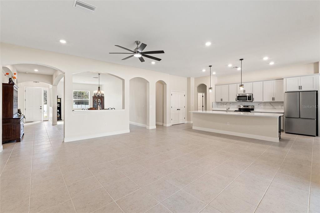 A spacious, open-concept kitchen and living area with tile floors, white cabinetry, and arched doorways — 14421 NONNA SKY DRIVE DRIVE, SPRING HILL, FL