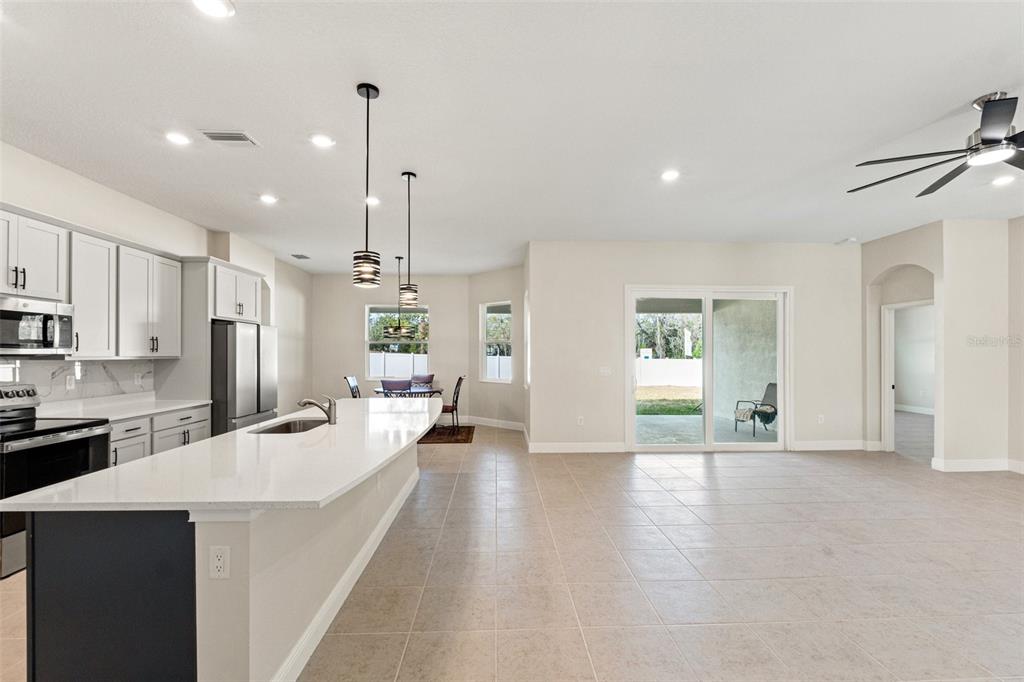 A bright, open-concept kitchen and living area featuring white cabinets, a quartz island, and tile — 14421 NONNA SKY DRIVE DRIVE, SPRING HILL, FL