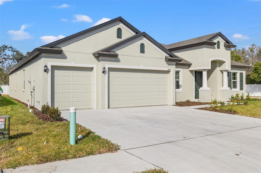 A single-story house with a three-car garage, light-colored stucco exterior, and a concrete driveway — 14421 NONNA SKY DRIVE DRIVE, SPRING HILL, FL