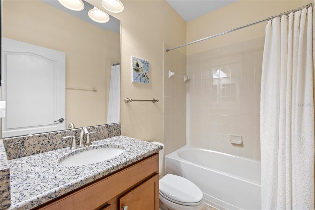 A bathroom features a granite vanity countertop, a single sink, and a shower-tub combination — 3801 SERENA LANE, CLERMONT, FL