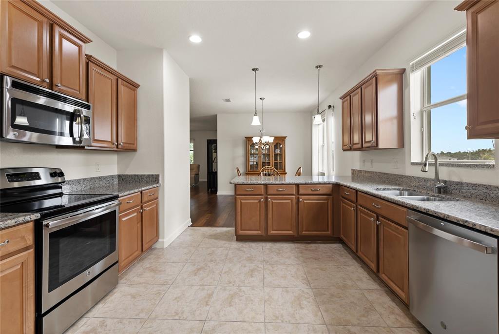 A kitchen with wood cabinets, granite countertops, stainless steel appliances, and tile flooring — 3801 SERENA LANE, CLERMONT, FL