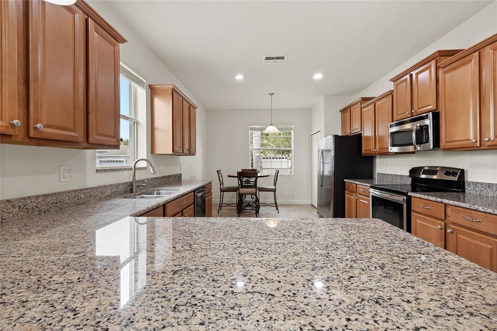 A kitchen with granite countertops, wooden cabinets, and a dining area with a table — 3801 SERENA LANE, CLERMONT, FL