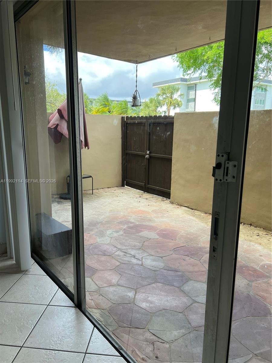 A view through a sliding glass door shows a paved patio with a wooden gate — 10845 SW 112th Ave # 107, Miami FL 33176, MIAMI, FL