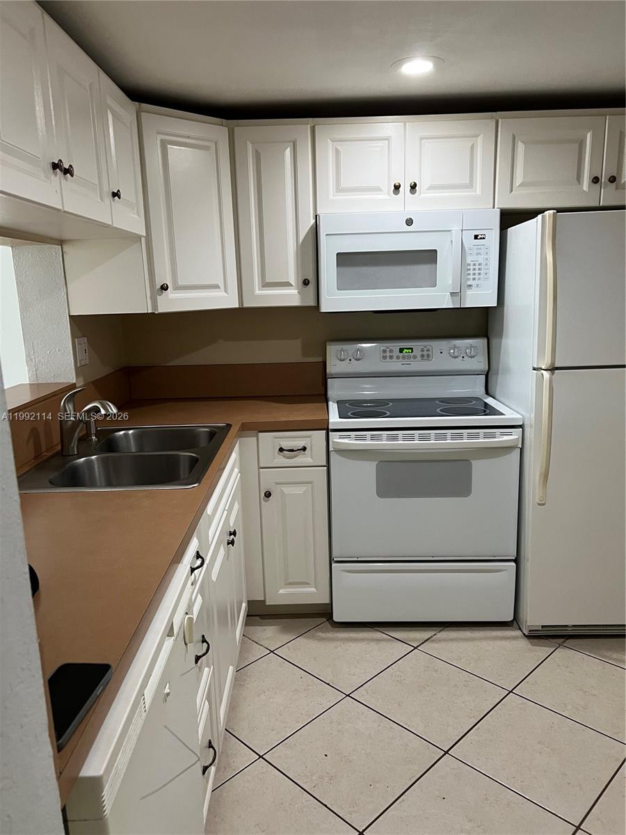 A kitchen features white cabinets, white appliances, a double sink, and tan countertops — 10845 SW 112th Ave # 107, Miami FL 33176, MIAMI, FL