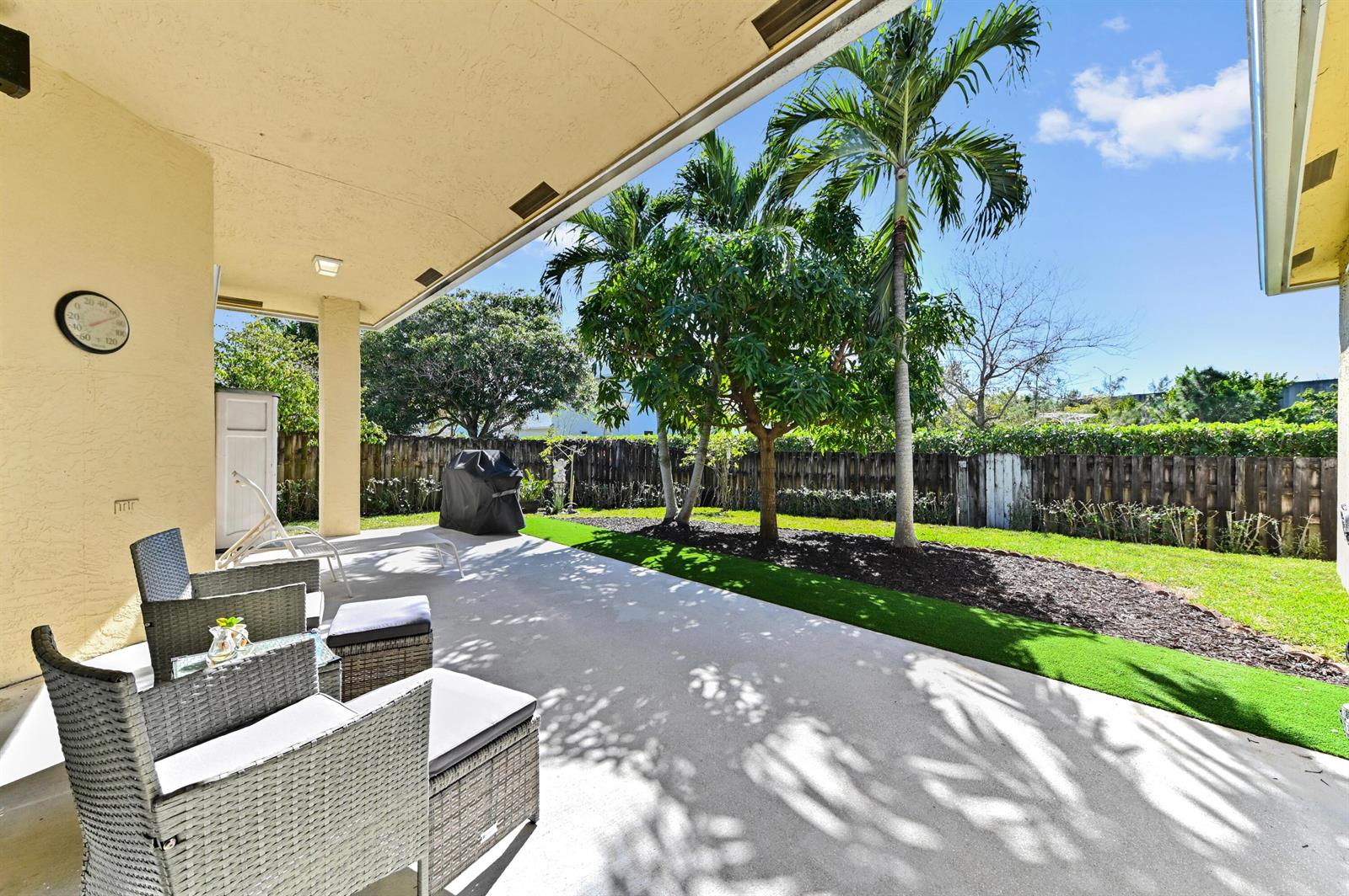 A covered concrete patio overlooks a backyard with artificial turf, palm trees, and a fence — 1791 Pierce Drive, FL 33460, FL