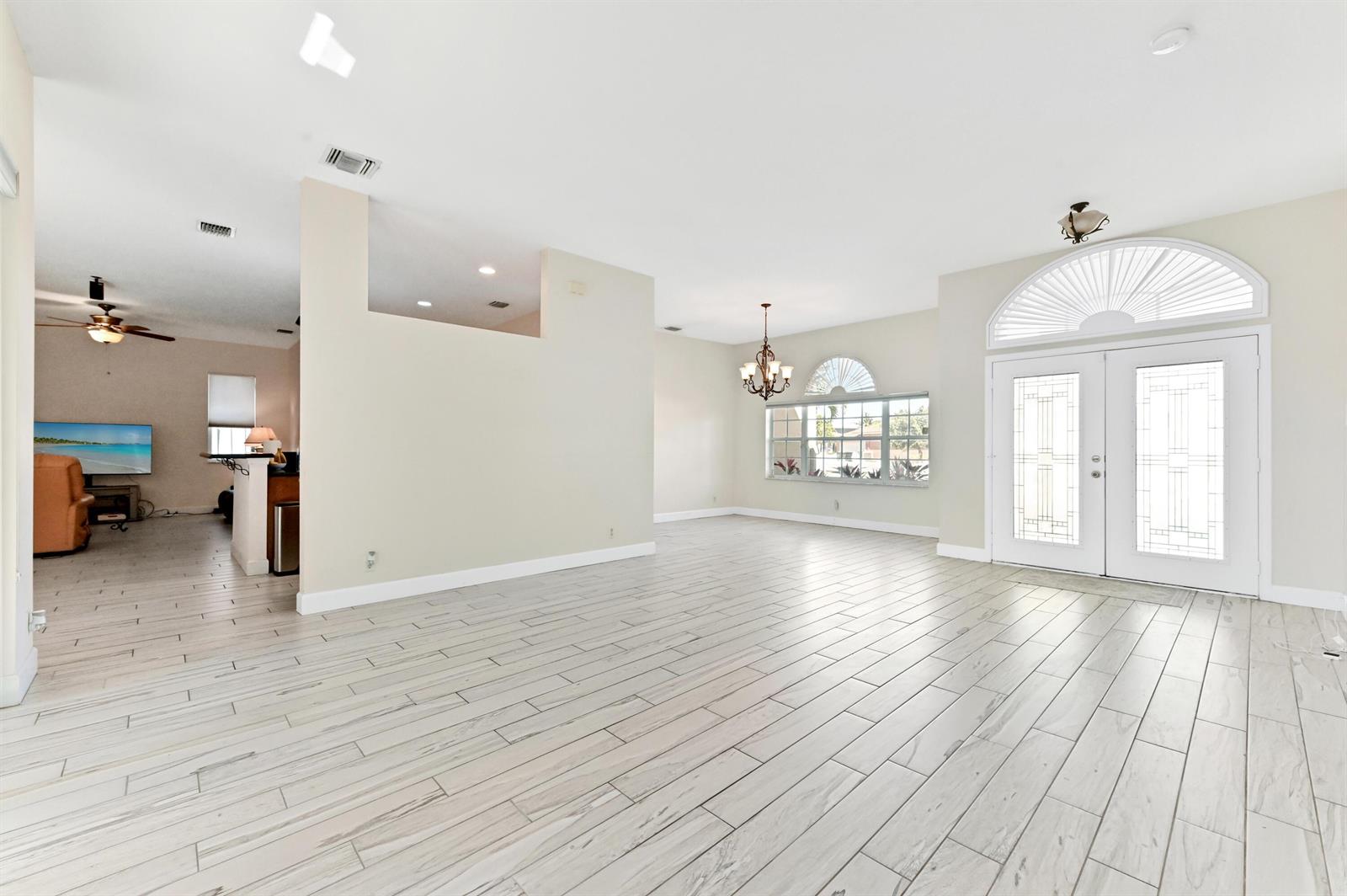 A bright, open-concept living area features light wood-look tile flooring and double glass entry doors — 1791 Pierce Drive, FL 33460, FL