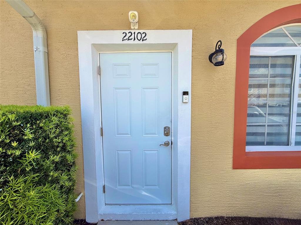 A light blue front door with a doorbell camera is set in a tan exterior wall — 22102 INDIAN CREEK DRIVE UNIT 1, KISSIMMEE, FL