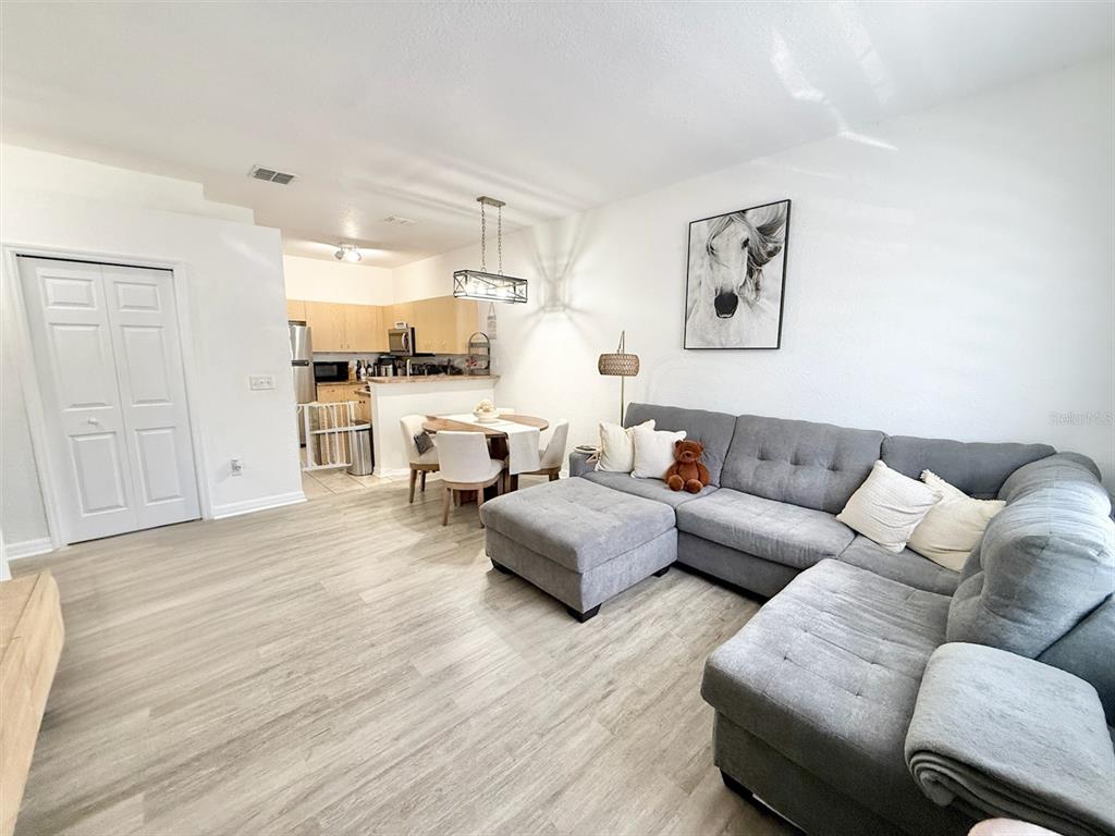 A living room with light wood-look flooring, a gray sectional sofa, and an adjacent dining area — 22102 INDIAN CREEK DRIVE UNIT 1, KISSIMMEE, FL