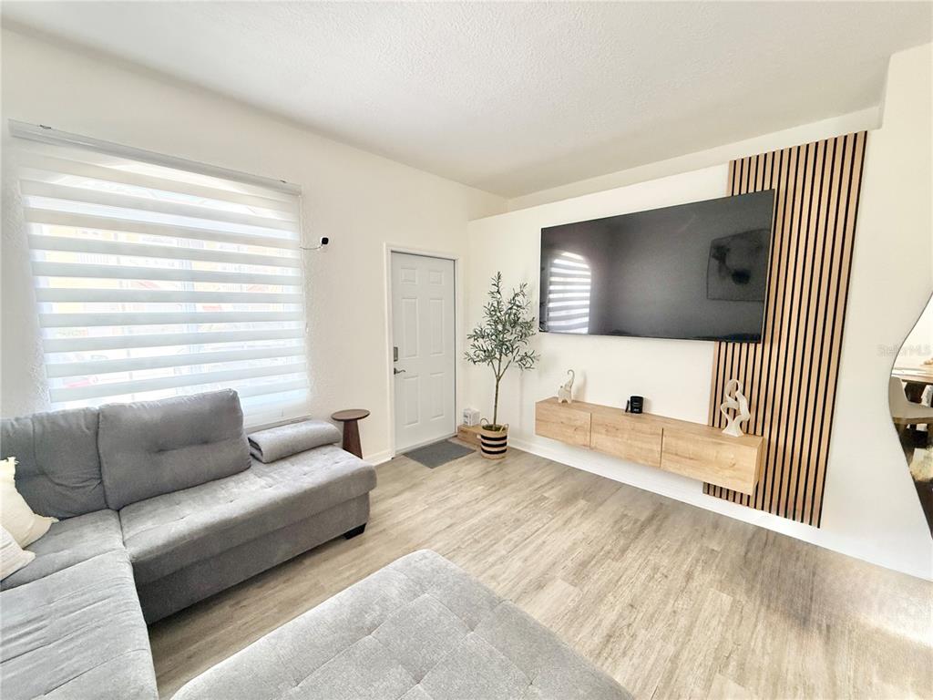 A living room features a grey sectional sofa, a wall-mounted television, and wood-slat accent paneling — 22102 INDIAN CREEK DRIVE UNIT 1, KISSIMMEE, FL