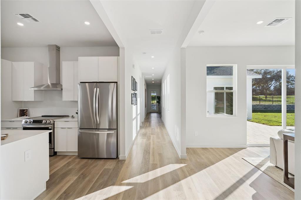 A modern kitchen with white cabinets and stainless steel appliances opens to a long hallway — 447 SKYFIELD COURT, LADY LAKE, FL