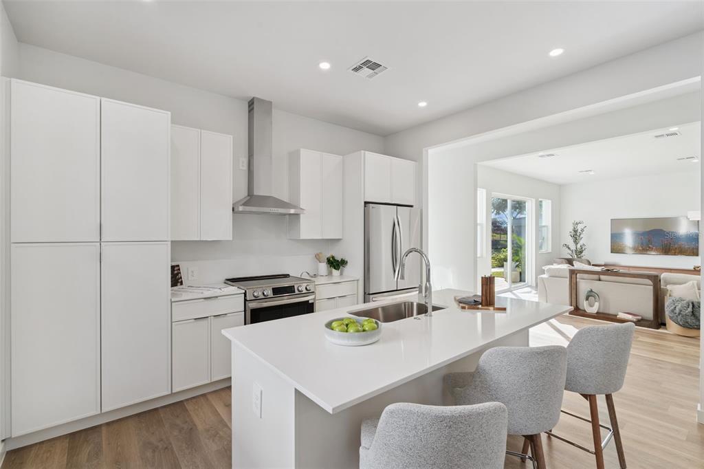 A modern kitchen features white cabinetry, stainless steel appliances, and a quartz-topped island with seating — 447 SKYFIELD COURT, LADY LAKE, FL