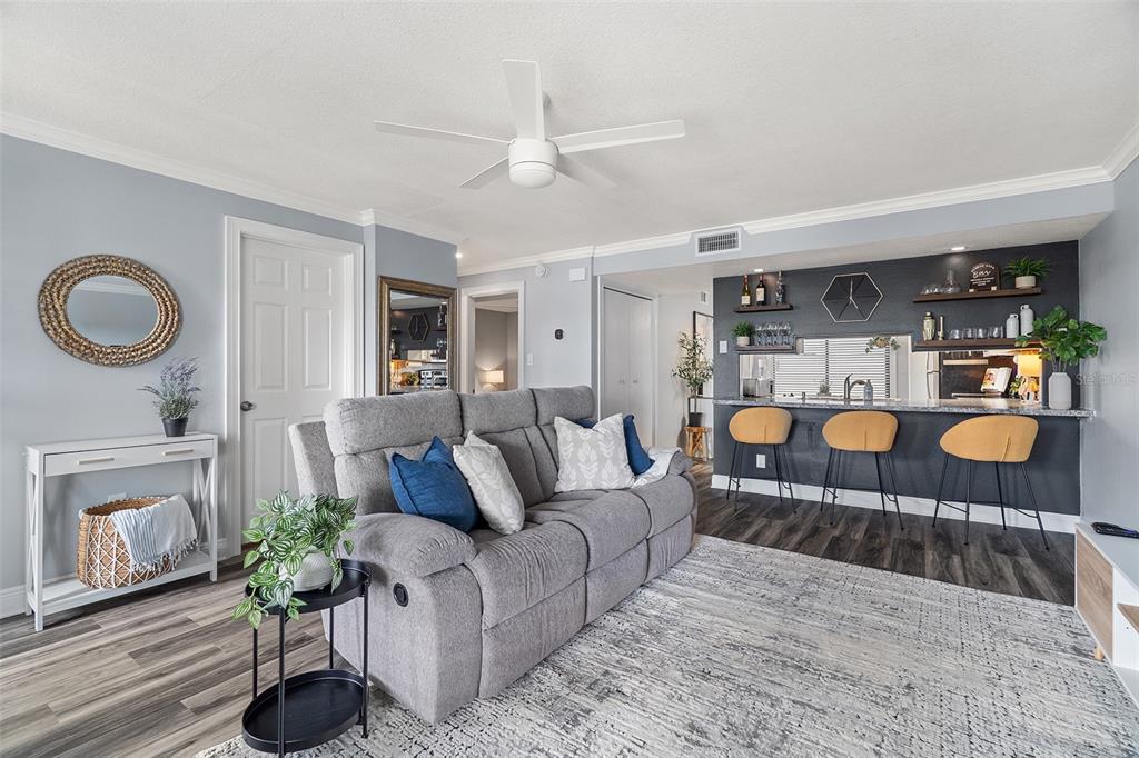 A living room features a gray sofa, a breakfast bar with stools, and wood-look flooring — 200 INTERNATIONAL DR UNIT 716, CAPE CANAVERAL, FL