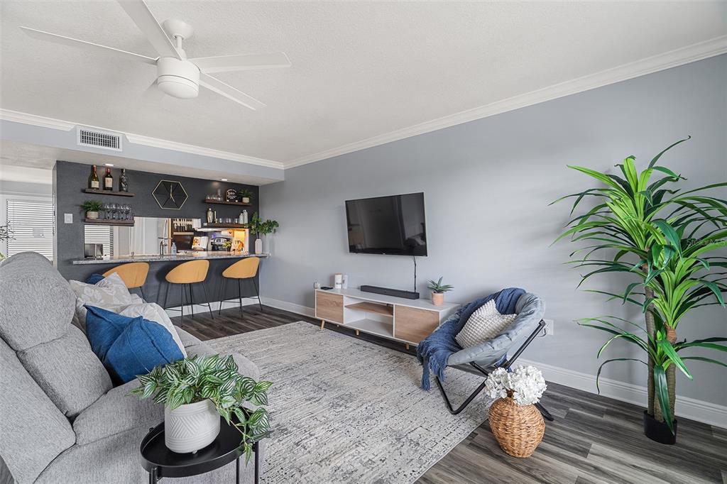 A living room features a gray sofa, a mounted television, and a kitchen bar area — 200 INTERNATIONAL DR UNIT 716, CAPE CANAVERAL, FL