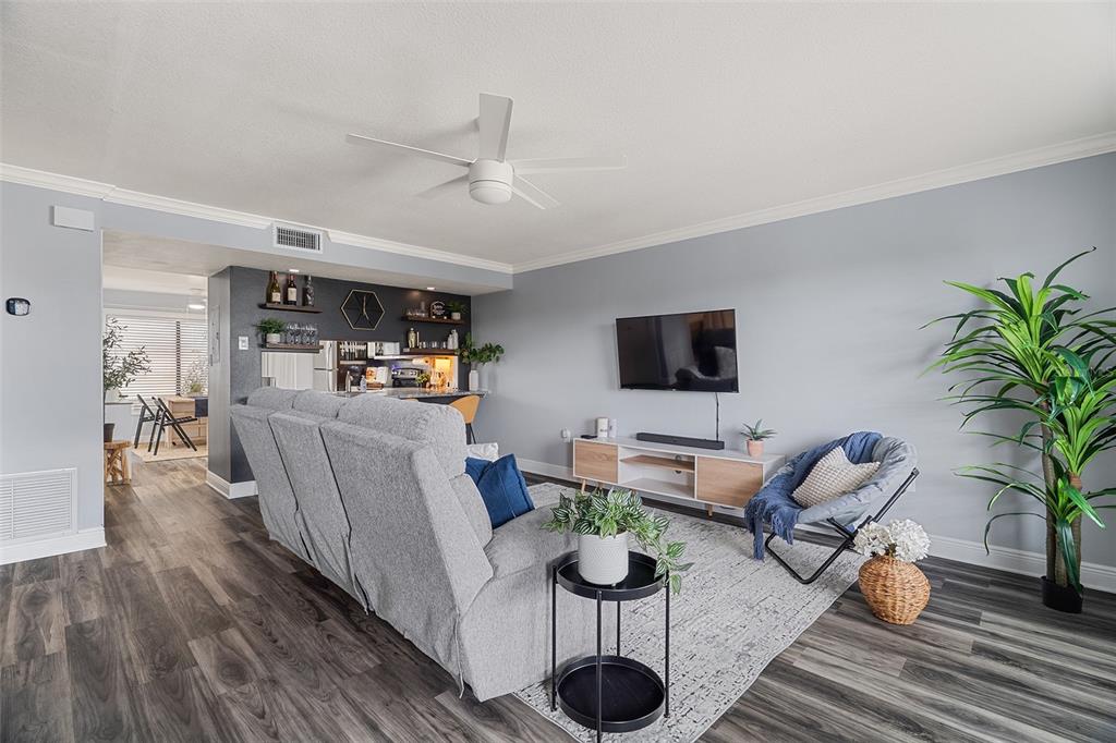 A living room features a grey sofa, a wall-mounted television, and wood-look flooring — 200 INTERNATIONAL DR UNIT 716, CAPE CANAVERAL, FL