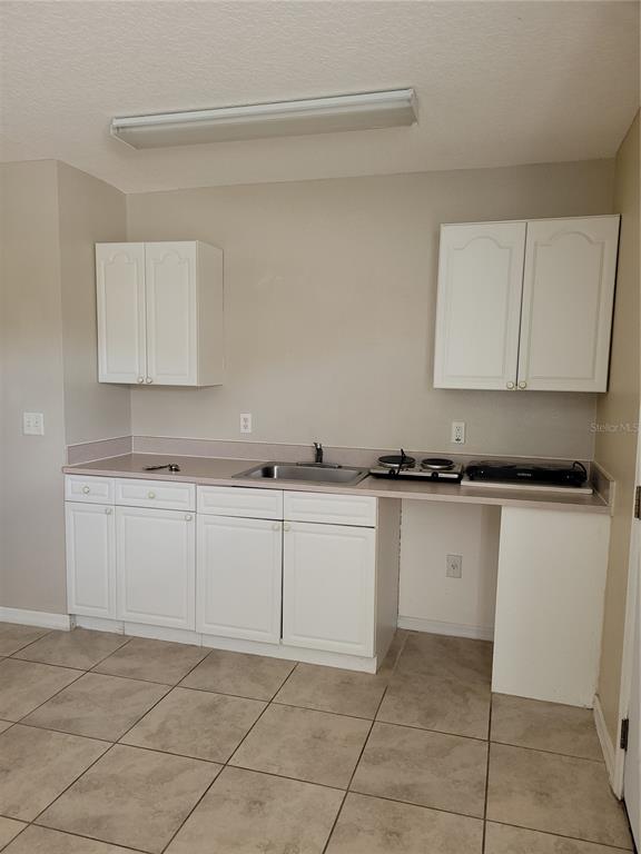 A small kitchen features white cabinets, a stainless steel sink, and tile flooring — 1325 WASHINGTON PALM LOOP, DAVENPORT, FL