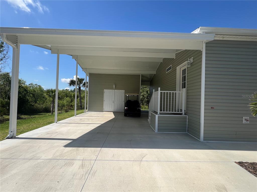 A concrete carport with a golf cart sits beside a house with light-colored siding — 12116 SW CR 769 SW COUNTY ROAD 769 UNIT 219, LAKE SUZY, FL