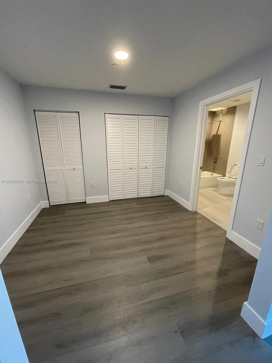 A bedroom features light gray walls, wood-look flooring, two sets of white louvered closets, and an attached bathroom — 1938 Jackson St # 301, Hollywood FL 33020, HOLLYWOOD, FL