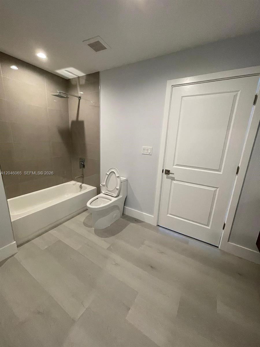 This bathroom features a white bathtub with a tiled wall, a toilet, and light-colored flooring — 1938 Jackson St # 301, Hollywood FL 33020, HOLLYWOOD, FL