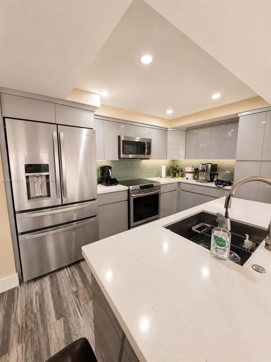 A modern kitchen features gray flat-panel cabinets, stainless steel appliances, and a white quartz island — 13380 SW 91st Ter, Miami FL 33186, MIAMI, FL