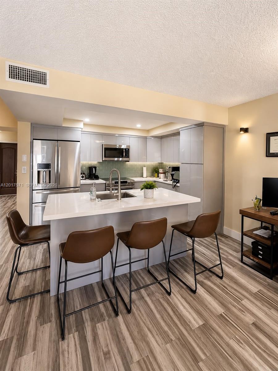 A kitchen features a white island with brown bar stools and grey cabinetry — 13380 SW 91st Ter, Miami FL 33186, MIAMI, FL