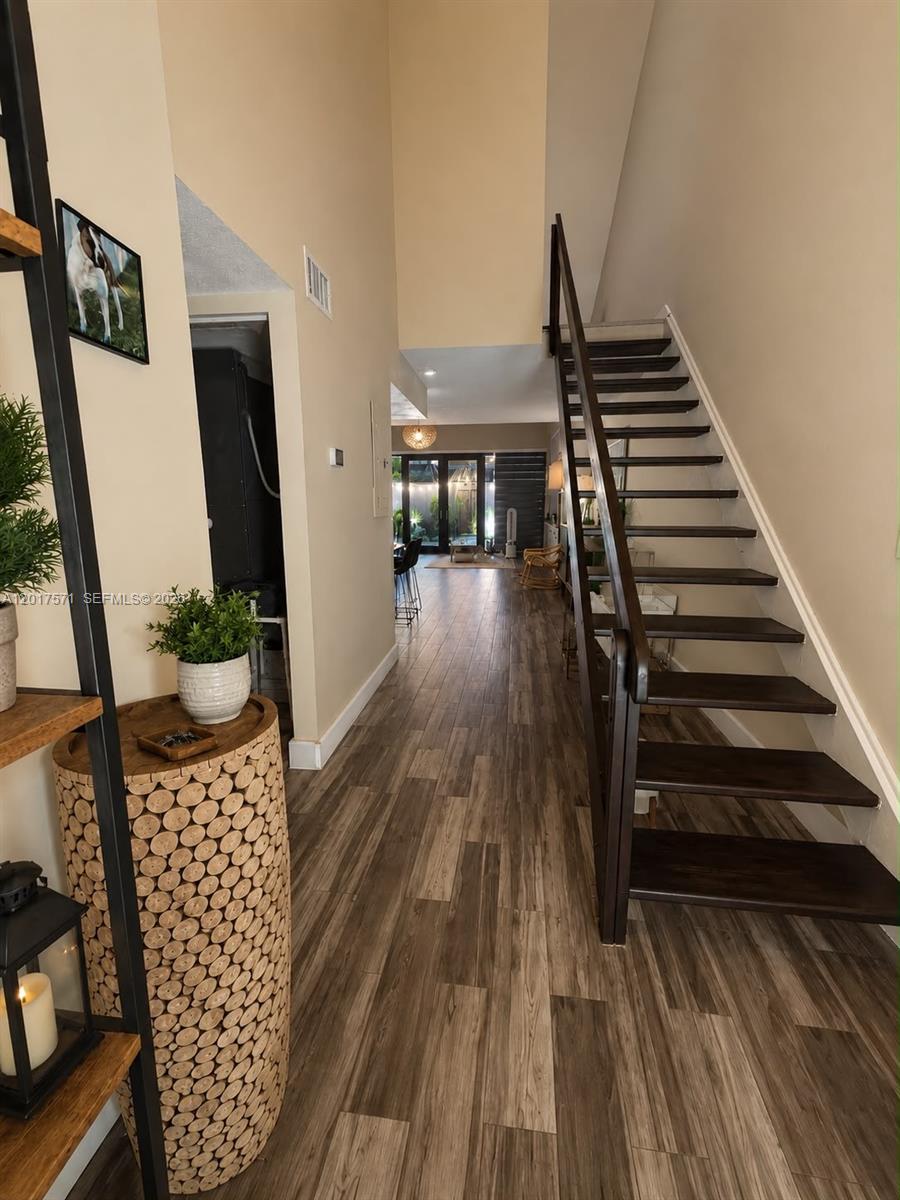 A hallway features wood-look flooring, a dark wooden staircase, and a textured cylindrical side table — 13380 SW 91st Ter, Miami FL 33186, MIAMI, FL